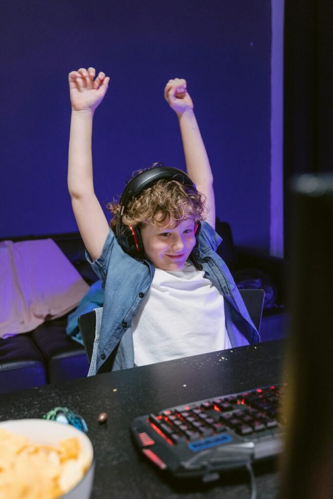 Child wearing headphones celebrates gaming victory with raised hands indoors.
